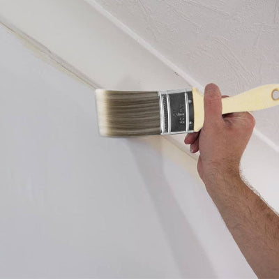 Main homme tenant pinceau peint angle mur plafond blanc