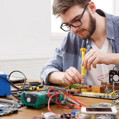 Jeune homme barbu lunette multitude circuits électroniques utilise tournevis jaune