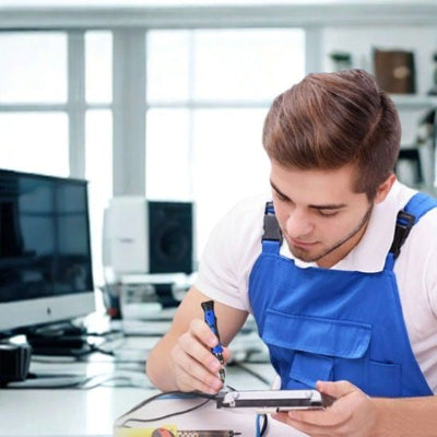 Jeune homme salopette bleue utilise tournevis tablette bureau ordinateur