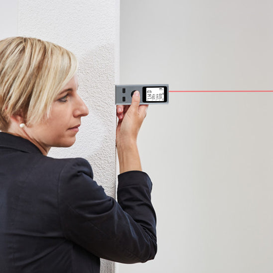 femme-de-profil-veste-noir-telemetre-laser-ecran-affichage-plaque-mur-blanc