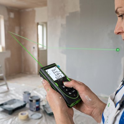 femme peintre tenue travail utilise télémètre laser faisceau vert pour mesurer mur dans pièce en cours de rénovation